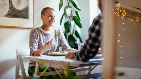 A woman with a shaved head smiles while eating a salad