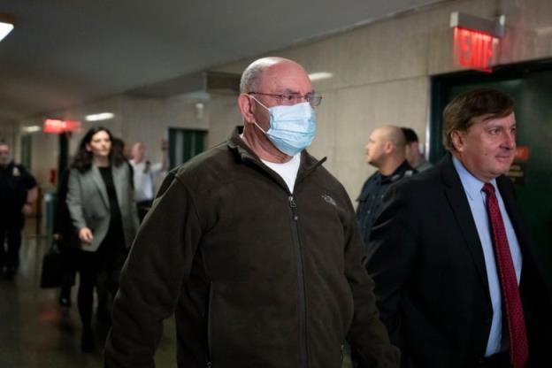 A man in a COVID-19 mask and a fleece zip-up sweater is shown walking in a hallway.