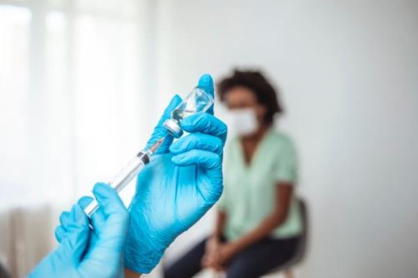 Doctor's hands in surgical gloves preparing COVID-19 vaccine for female patient. Female doctor pulling COVID-19 vaccine liquid out from vial with syringe. Prevention and immunization from corona virus infection