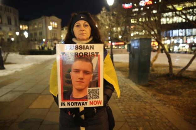 A woman stands with a poster of Andrei Medvedev's face and the text 'Russian terrorist in Norway now.'