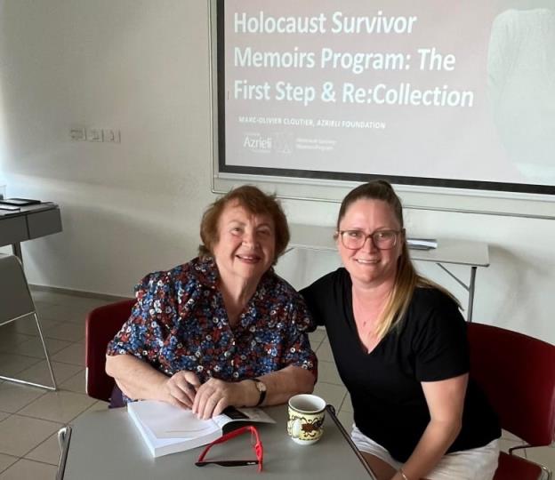 Two women smile for a photo as they sit in a classroom space. A projected screen behind them reads The Azrieli Foundation Holocaust Survivor Memoirs Program.